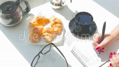 年轻漂亮的女孩在阳光明媚的日子里吃早餐，在笔记本上写一封信